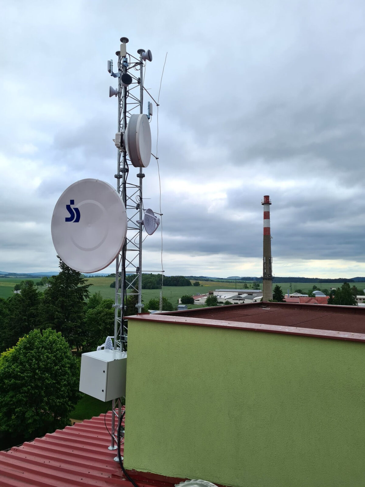 Příhradový stožár s anténami na střeše budovy pod zataženou oblohou
